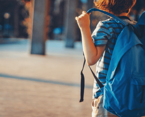little boy in striped shirt wearing a blue backpack ready for back to school season