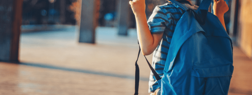 little boy in striped shirt wearing a blue backpack ready for back to school season